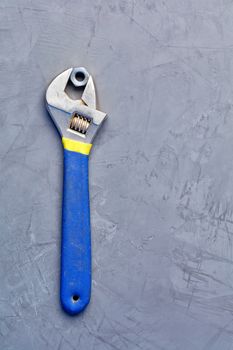 In an old adjustable wrench with a rubberized blue handle, an old metal nut is clamped, an image against a gray concrete background, with copy space.