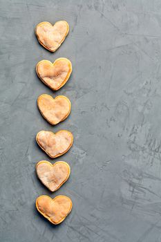 Delicious homemade gingerbread shortbread cookies in the shape of unpresentable hearts laid out vertically in a row on a gray concrete surface, image with copy space.