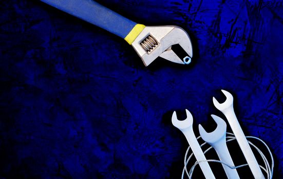 An old adjustable wrench teaches skill and provides food for new open-end wrenches, classic dark blue color background. The concept of communication and training, image with copy space.