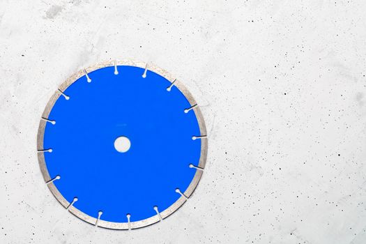 Cutting blade blue color with diamond for cutting reinforced concrete using an angle grinder on a gray concrete background, image with copy space.