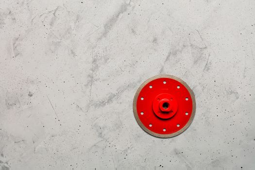 Cutting disc red color with diamond, a thin blade of diameter of 125 mm with a flange is used for precise cutting of the material against the background of gray concrete, image with copy space.