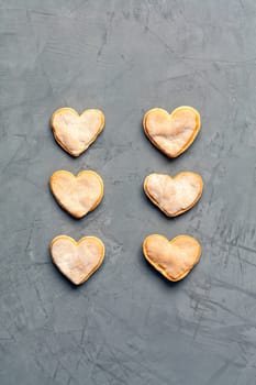 Delicious homemade gingerbread cookies in the shape of hearts laid out vertically in a row on a gray concrete surface, image with copy space.