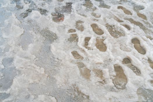 Traces of shoes in slush. The sidewalk is covered with melted snow.