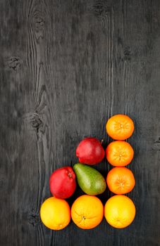 Ripe oranges, tangerines, apples, avocados lie on an old black wooden surface, flat lay, image with copy space.