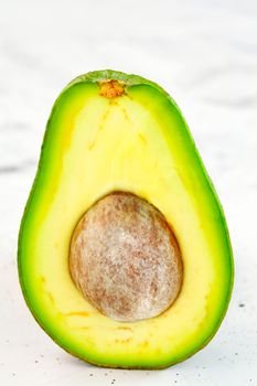 Avocado cut in half, one slice with core on gray concrete background, close-up. Delicious and nutritious fruit, image with copy space.