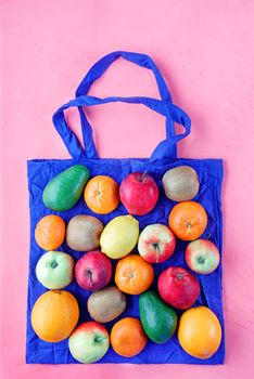 Eco-friendly cotton bag in blue color against a pink color background. Zero waste concept, plastic-free, eco-friendly shopping with fruits and vegetables, image with copy space.