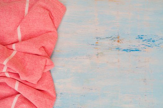 Red and white kitchen towel lies on wooden table. Texture of painted wood. Textured fabric folds.