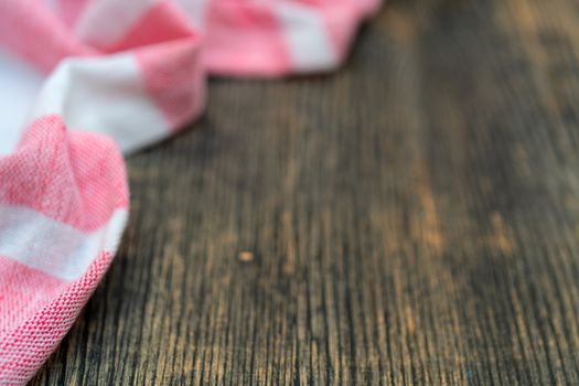 Red and white kitchen towel lies on wooden table. Texture of painted wood. Textured fabric folds.