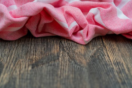 Red and white kitchen towel lies on wooden table. Texture of painted wood. Textured fabric folds.