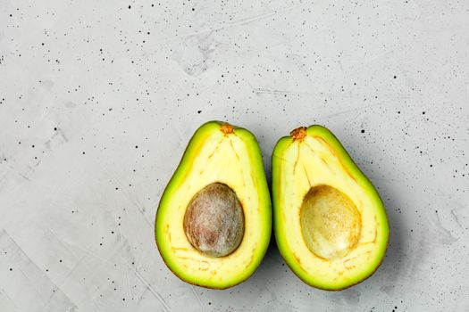 Avocado cut in half, one slice with core on gray concrete background, close-up. Delicious and nutritious fruit, image with copy space.