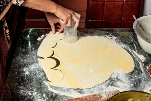 Female hands prepare round dough blanks for modeling dumplings in Ukrainian national cuisine.