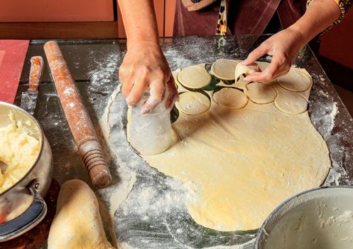 Housewife hands preparing round dough pieces for modeling dumplings in Ukrainian national cuisine.