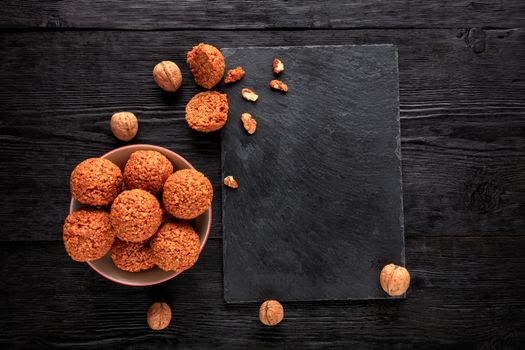 Homemade energy balls with walnuts, peanuts, honey and banana in a porcelain plate on a black wooden background,. Vegan vegetarian raw snacks. Healthy sweet food. Low key. Copy space flat lay, top view.