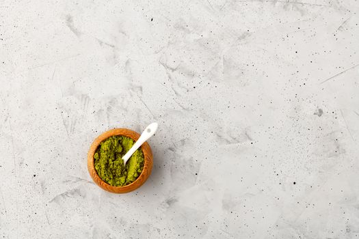Matcha green tea powder in oak cup with white ceramic spoon on gray concrete background, flat lay, copy space.
