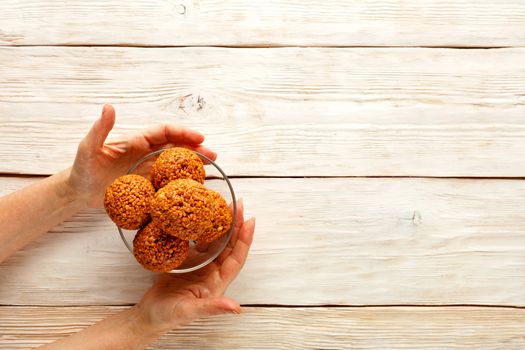 Homemade energy balls with walnuts, peanuts, honey and a banana in a glass bowl, housewife puts on a light wooden table. Copy space. Flat lay, top view.