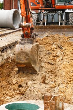 A road service excavator digs a trench on the roadway to replace old concrete blocks with new wells and sewer pipes.