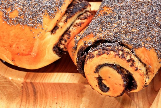 Ruddy fresh rolls with poppy seeds lies on wooden tray on wooden surface closeup, flat lay.