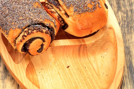 Ruddy fresh rolls with poppy seeds lies on wooden tray on wooden surface closeup, copy space.