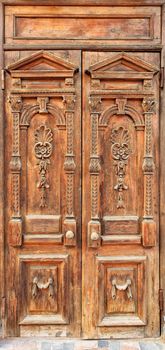 Old wooden entrance doors with carved elements framed on the facade with a carved symmetrical pattern from top to bottom.