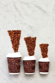 Coffee beans and three disposable cardboard mugs of different capacities for hot drinks, with a lid on a gray concrete background, vertical image, copy space.