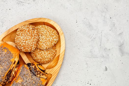 Homemade fresh buns with poppy seeds and cookies with sesame seeds on a wooden kitchen board, on a background of gray concrete, closeup, copy space.