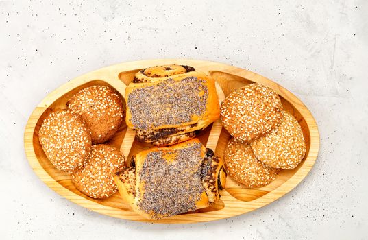 Fresh buns with poppy seeds and cookies with sesame seeds on a wooden surface, on a background of gray concrete, close-up, copy space.
