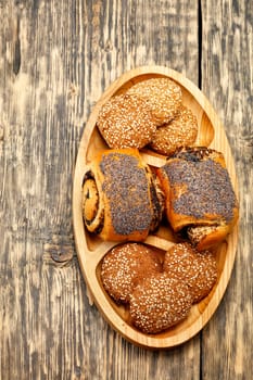 Homemade fresh buns with poppy seeds and cookies with sesame seeds on a wooden oval board, on a old wooden surface close-up, closeup, copy space, vertical image.
