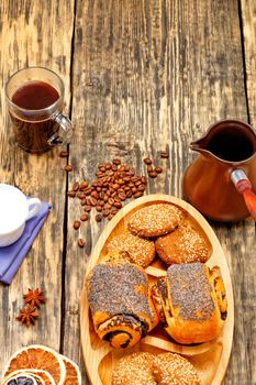 Coffee beans are scattered on an old wooden table and freshly brewed coffee in transparent glass cup to anise stars, next to a coffee teapot, cream and homemade fresh buns in slight blur.