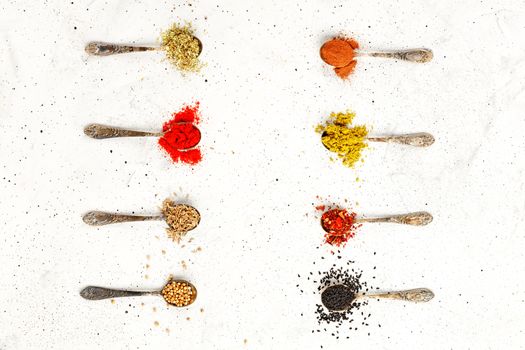 Old silver spoons with various asian spices mayran, caraway, cinnamon, hops, zira, allspice, ground paprika, corinade on a gray concrete background. Top view,, copy space.