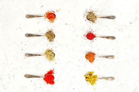 Old silver spoons with various asian spices mayran, hops, saffron, sumy, ground paprika, cinnamon, basil, oregano on a gray concrete background.