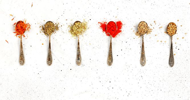Old silver spoons with various asian spices saffron, zira, corinade, ground paprika, mayran, oregano on a gray concrete background.
