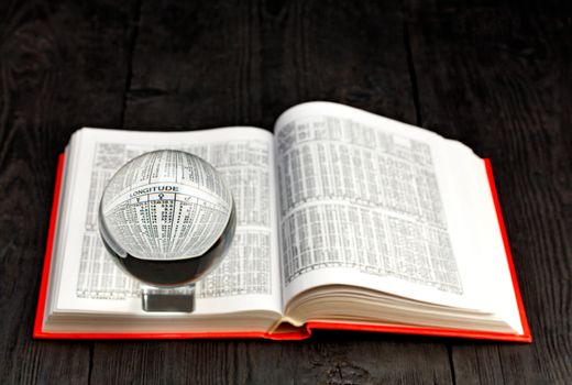 Crystal ball and open book of ephemeris in bright red binding on an old black wooden table background, copy space.