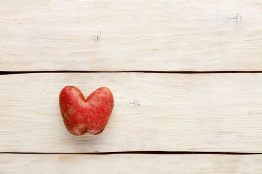 Ugly funny vegetables, heart-shaped potatoes on a white wooden background. The concept of grungy vegetables or food waste. Top view, copy space.