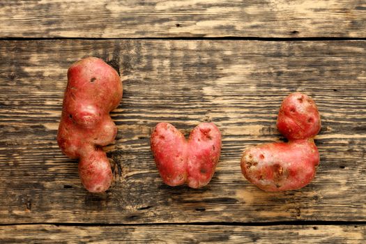 Ugly funny vegetables, heart-shaped potatoes and letter shape on a brown wooden background. The concept of grungy vegetables or food waste. Top view, copy space.