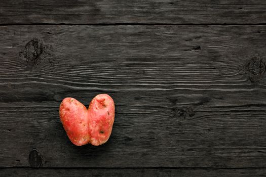 Ugly funny vegetables, heart-shaped potatoes on a black wooden background. The concept of grungy vegetables or food waste. Top view, copy space.