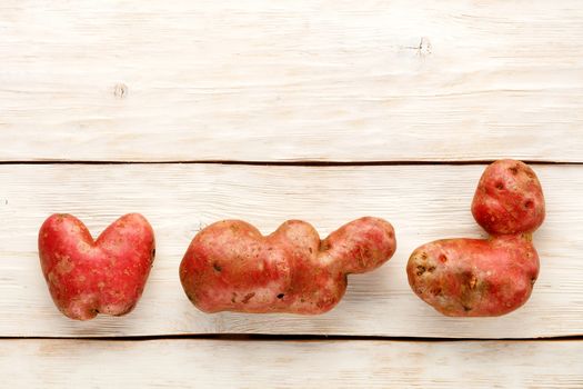 Ugly funny vegetables, heart-shaped potatoes and letter shape on a white wooden background, close-up. Top view, copy space.