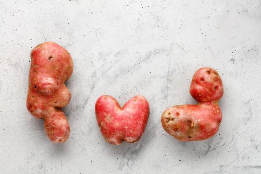 Ugly funny vegetables, heart-shaped potatoes and letter shape on gray concrete background. The concept of grungy vegetables or food waste. Top view, copy space.