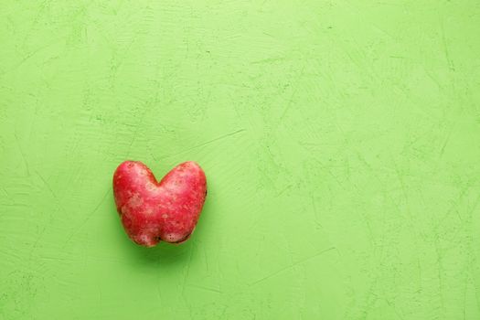 Ugly funny vegetables, heart-shaped potatoes on a green concrete plaster background. The concept of grungy vegetables or food waste. Top view, copy space.