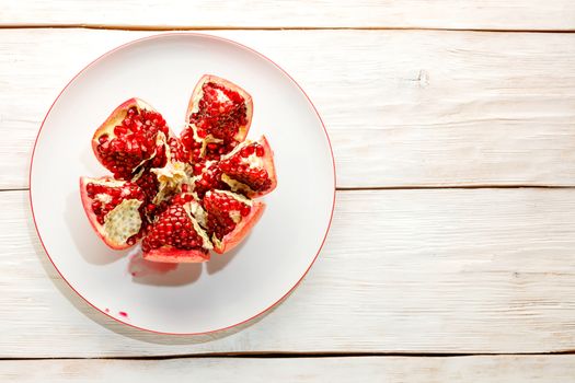 Ripe and red pomegranate fruits and divided into pieces on a white porcelain plate on a wooden white background.
