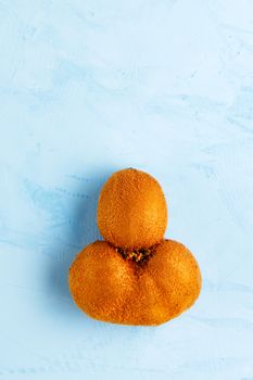 Green ripe funny kiwi with a brown peel whole on a blue stucco shows up. Top view, horizontal image, copy space.