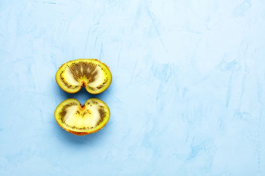 Green ripe kiwi on a blue plaster surface is cut in half, a beautiful pattern of the inner green pulp of the fruit. Top view, copy space.