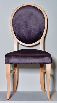 Classic wooden chair with soft dark purple upholstery and a round back, photographed in front, on a gray podium and background.