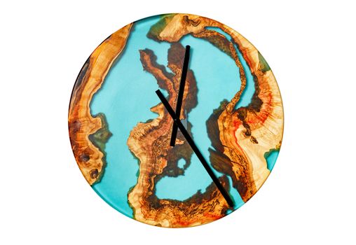 Beautiful wooden wall clock made of cut roots of a tree and translucent turquoise-colored epoxy on a dial in the form of land and sea on a white background isolated.