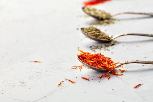 Saffron seasoning in an old silver spoon on the background of other spices in blur on a gray concrete background. Side view, copy space.