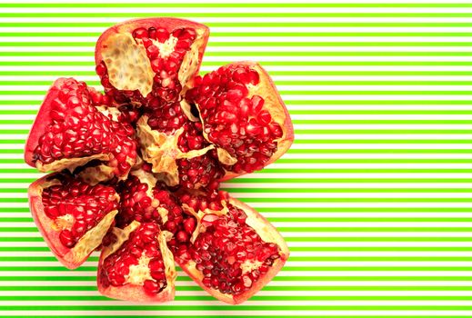 Ripe and red pomegranate fruits and are divided into parts, on a striped light green and white background, close-up, copy space, top view.