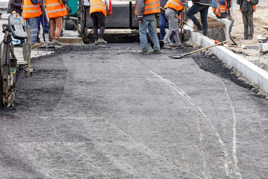 The working group of road workers updates the stretch of road with fresh hot asphalt and smoothes it to repair the road surface of the roadway, copy space,