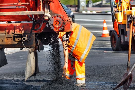 A road service worker accepts the unloading of fresh asphalt from a car for subsequent repair of a section of the road.