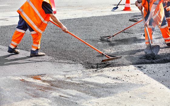 The road workers' working group updates part of the road with fresh hot asphalt and smoothes it for repair with a metal levels and shovels.