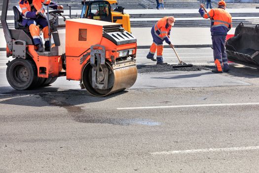 Road service workers use a vibratory roller, a road bulldozer and a metal level to repair the pavement and compact the asphalt.