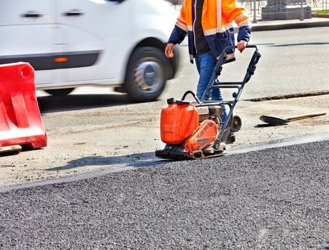 A road worker compacts asphalt on the carriageway with a gasoline vibratory compactor.